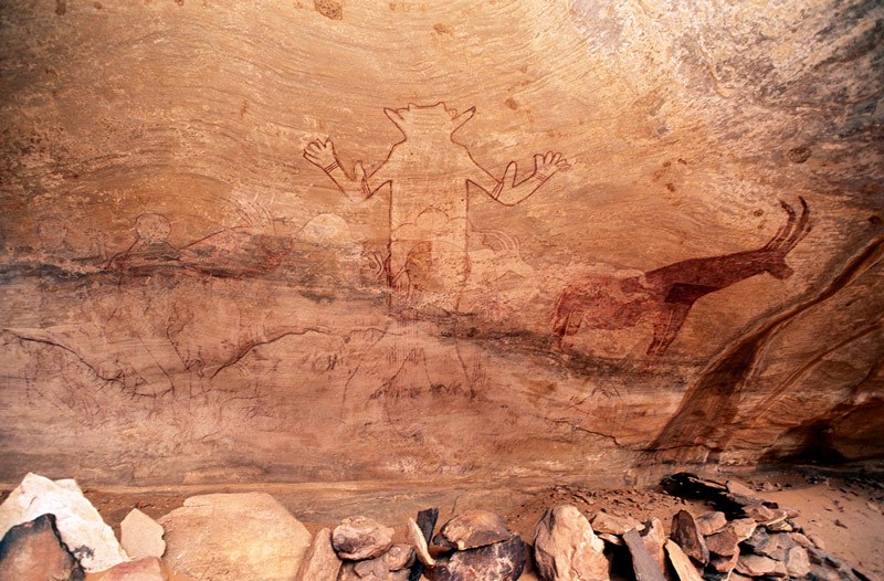 Djanet, Algeria. Close-up of painting, Note how huge mythical figure positioned so that curved layers in rock surface flow out and up on either side of head and body. Image ID: algdja0020009