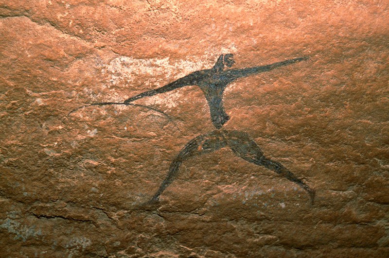 Oued Djaret, Algeria. Man faces forward with arms and legs widespread. He wears white skullcap with chinstrap, belt and tight decorated trousers and shirt, or has decorated body markings. Holds bow in one outstretched hand. Possible cloth flows right from waist. (Archer used by Trust for African Rock Art as Trust’s logo.) Image ID: algdja0050031