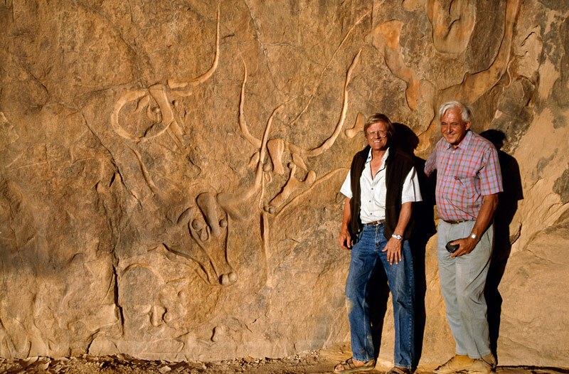 Djanet, Algeria. Trust for African Rock Art’s recording team, David Coulson (left) and Alec Campbell standing standing next to cattle engravings. Image ID: algdja0060010