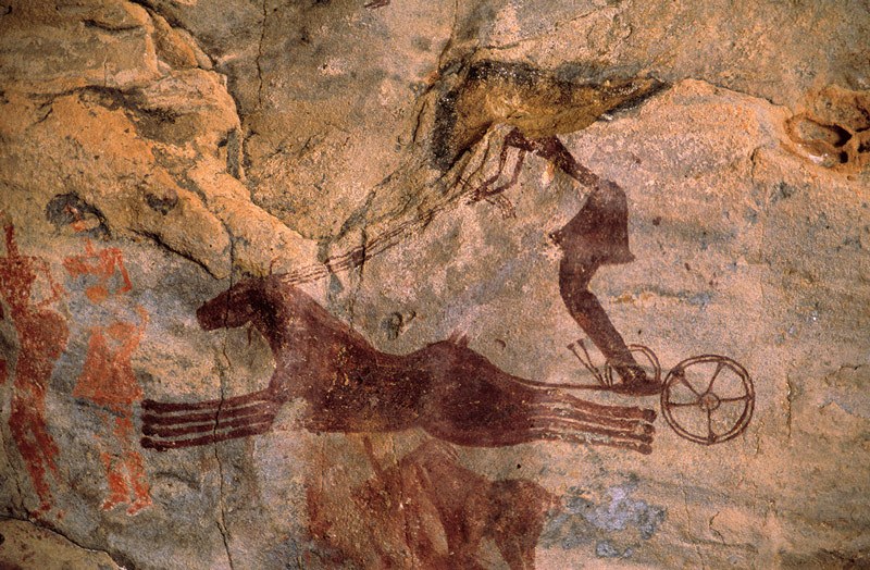 Tarssed Jebest, Algeria. Maroon painting of two horses galloping to left drawing chariot with charioteer wearing skirt and holding four reins. Image ID: algtdj0010047