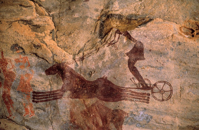 Tarssed Jebest, Algeria. Maroon painting of two horses galloping to left drawing chariot with charioteer wearing skirt and holding four reins. Image ID: algtdj0010047
