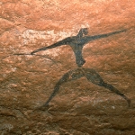 Oued Djaret, Algeria. Man faces forward with arms and legs widespread. He wears white skullcap with chinstrap, belt and tight decorated trousers and shirt, or has decorated body markings. Holds bow in one outstretched hand. Possible cloth flows right from waist. (Archer used by Trust for African Rock Art as Trust’s logo.) Image ID: algdja0050031