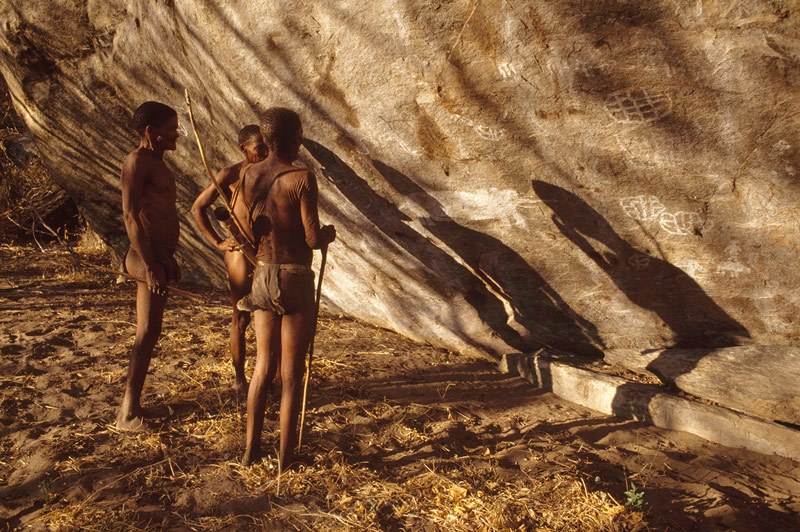 Tsodilo Hills. Three Zhu Bushmen examine white paintings in White Paintings Shelter. Image ID: bottsd0520001