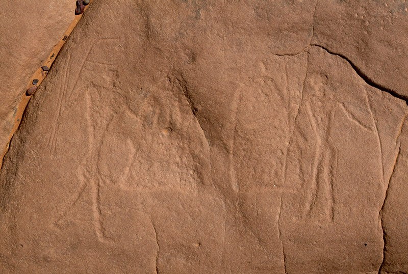 Ennedi Plateau. Block-pecked engraving of two men facing each other, each holding a shield and spear. Horse/Camel Period. Image ID: chaenp0010104
