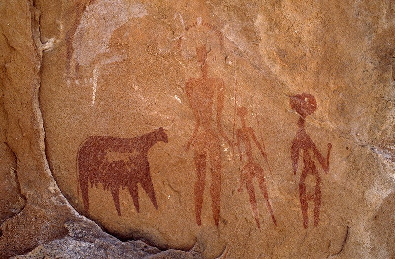 Ennedi Plateau. Faded bichrome cow with white udder facing right. Two faded men facing forwards. Tall man has headdress and holds spear. Short man has round head with three plumes, back-skirt, and holds spear. Third man painted in maroon has burden on head and holds club. Bichrome red cow with udder and white horns. Small antelope facing right superimposed on red cow. Image ID: chaenp0040008
