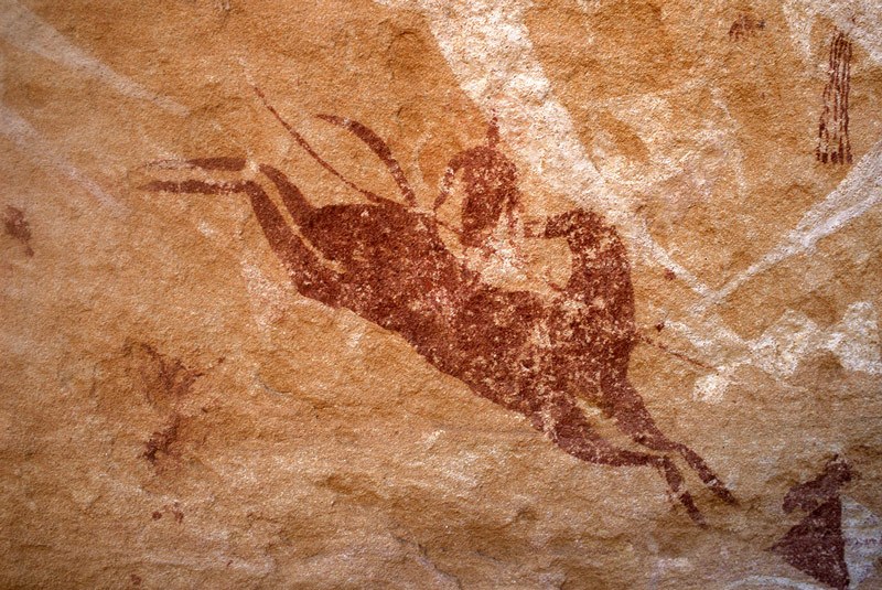 Ennedi plateau. White ‘running’ shapes superimposed by red leaping horse with head turned back mounted by red man holding long spear. Bottom right, bichrome shield. Top right, red camel-saddle trappings. Image ID: chaenp0050016