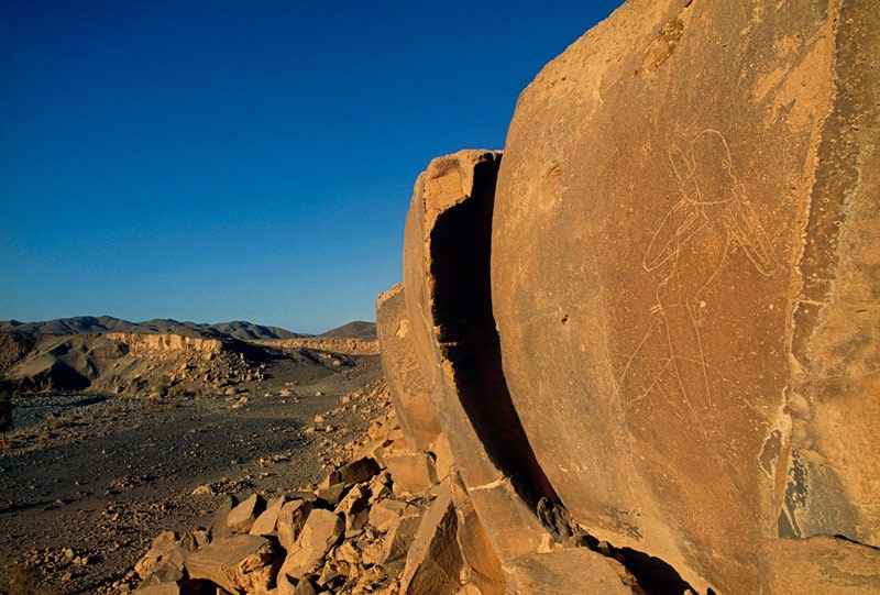 Tibesti Mountains. Known as ‘L’Homme de Gonoa’, an ‘Early Hunter Period’ engraving of a man (2 metres high) holding a mask to his face and running to the right. (Note the recently added graffiti – pubic hair and air coming from the anus). Image ID: chatim0020025