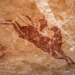 Ennedi plateau. White ‘running’ shapes superimposed by red leaping horse with head turned back mounted by red man holding long spear. Bottom right, bichrome shield. Top right, red camel-saddle trappings. Image ID: chaenp0050016