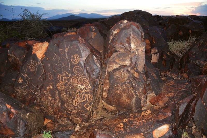 Lokori. Boulders on tabletop. Middle boulder has fairly recently pecked engravings: circles, concentric circles joined to spiral, three joined spirals, circle containing bar, circle containing cross, oval with bar. Image ID: kenlok0010015
