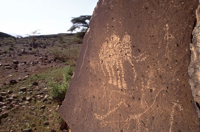 Turkana. Engraving of an elephant facing right. To the right of the elephant is a human figure and below the elephant to the right are humans and giraffes. Image ID: kentur0010002