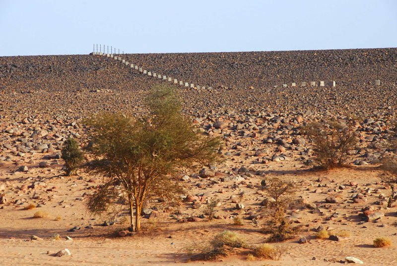 Messak. Ugly concrete & iron fence marking perimeter of main Wadi Mathendous rock art site. Image ID: libmes0170003
