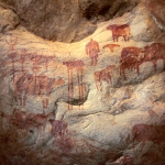 Tagant, Mauritania. On bulge between back wall and roof of shelter, thickset red man facing forwards, red cows, red cow with elongated legs, red shape (predator?), red tridents on vertical crossed bars. Image ID: mautag0080024