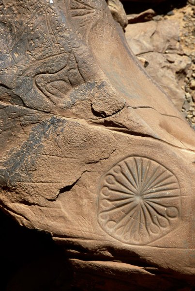 Atlas Mountains, Morocco. Rock with Tazina-style engravings of antelope and spoked wheel placed in homestead courtyard wall. Image ID: moratm0010211