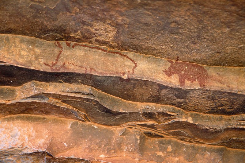 Aar Farm, Namibia. Outline red finger-drawn painting of rhinoceros facing left; and solid red painting of rhinoceros facing left. Image ID: namsna0020006
