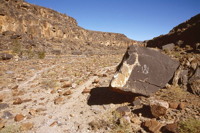Huns Mts, Namibia. Looking south down Nuab River. Boulder in foreground with modern graffiti. Head and upper body of person with hands raised. Image ID: namsnh0030053