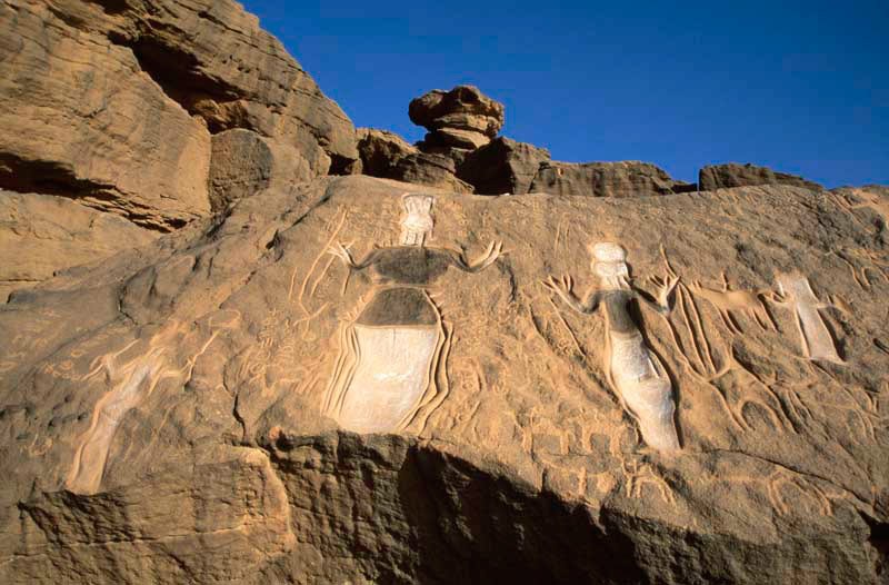 Northern Air Mountain. Two large engraved figures with raised hands and objects/headdress on heads face forwards. Probably, figures originally carved in Libyan Warrior style, but more recently ground out and interiors painted in blue-black and white. Image ID: nignam0020017