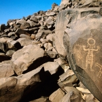 Air Mountain, Niger. Pecked engraving of Warrior with round head, dangling earrings, ‘leather’ suit and hands raised standing next to small horse. Second more-recent crudely pecked man. Image ID: nigeam0010024