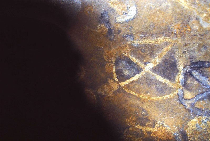 Dhayamole. Oval containing diagonal cross and part orange circle containing cross, both outlined in black. Image ID: somdha0020043