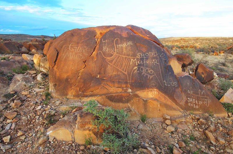 Morodi. Half-buried, granite boulder on low ridge. At left, pecked engraving of schematic cow superimposed by graffiti. Image ID: somgab0100021