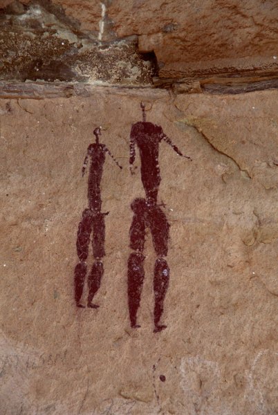 Drakensberg, South Africa. Two men, naked except for beaded arm and bicep bands, stand in twisted perspective looking right. Both men have blank faces and erect penises. Taller man’s penis is infibulated. Both men have ring of beads on hips. Image ID: soadrb0080037