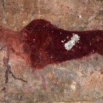Drakensberg, South Africa. Large, finely-painted, red eland walks left with man holding bow, also walking left, superimposing eland’s neck. Note vandalism. Red painted has been chipped out, (usually to include in medicine to make rain or bring health). Image ID: soadrb0080041