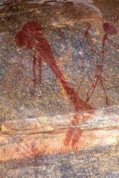 Large red figure facing left, bent at waist, arms hanging, animal’s head with hair on end, Yellow giraffe in background. Image ID: tankon0030007