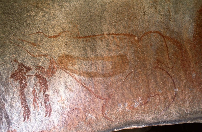 Mashonaland, Zimbabwe. Large crocodile, with scales shown along outline, lies on back with stream of blood issuing from rear leg. Orange geometric shape on stomach. Three men stand at left, one below almost vertical mythical animal. Image ID: zimmsl0170004