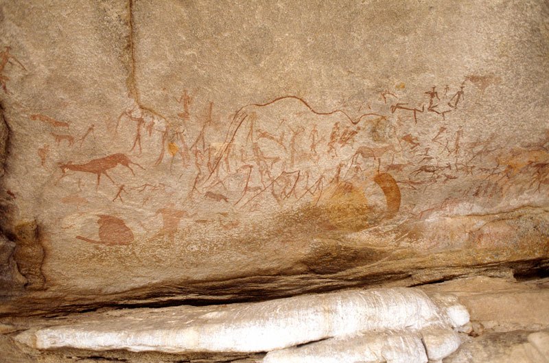 Mashonaland, Zimbabwe. Across top, large faded white paintings of animals facing left (antelope, predator, hippo) superimposed by red paintings of people standing, seated, lying with animals’ heads, holding objects, dancing, falling, and associated with animals. Image ID: zimmsl0270013